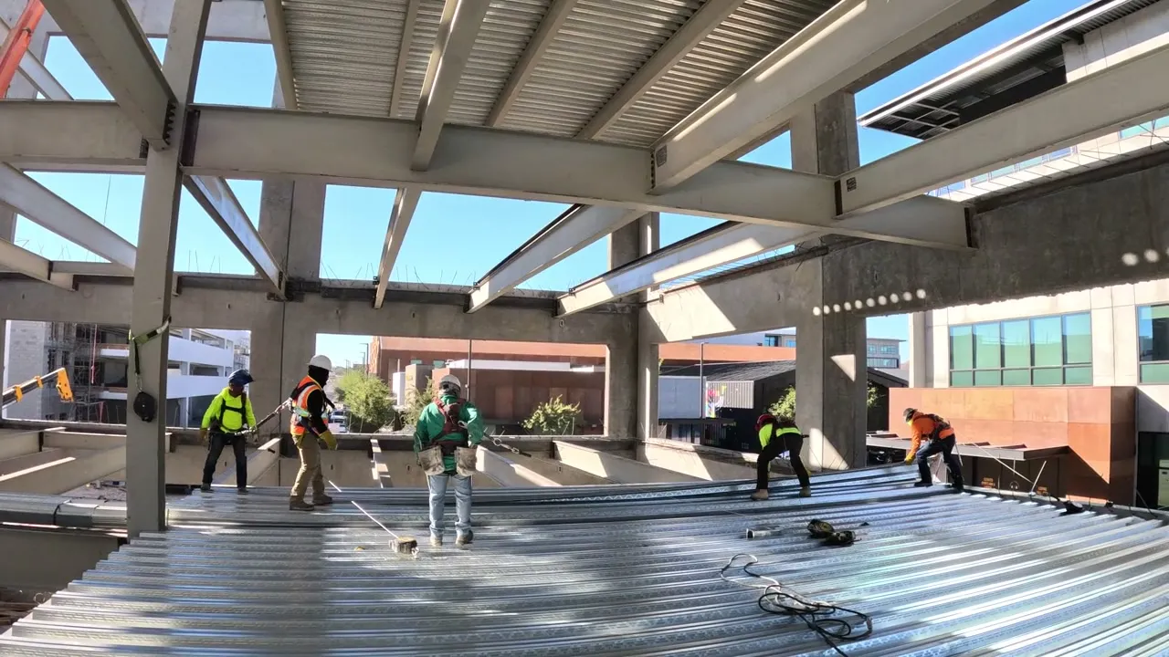 Ironworkers in hard hats and harnesses working a new metal deck under a steel frame